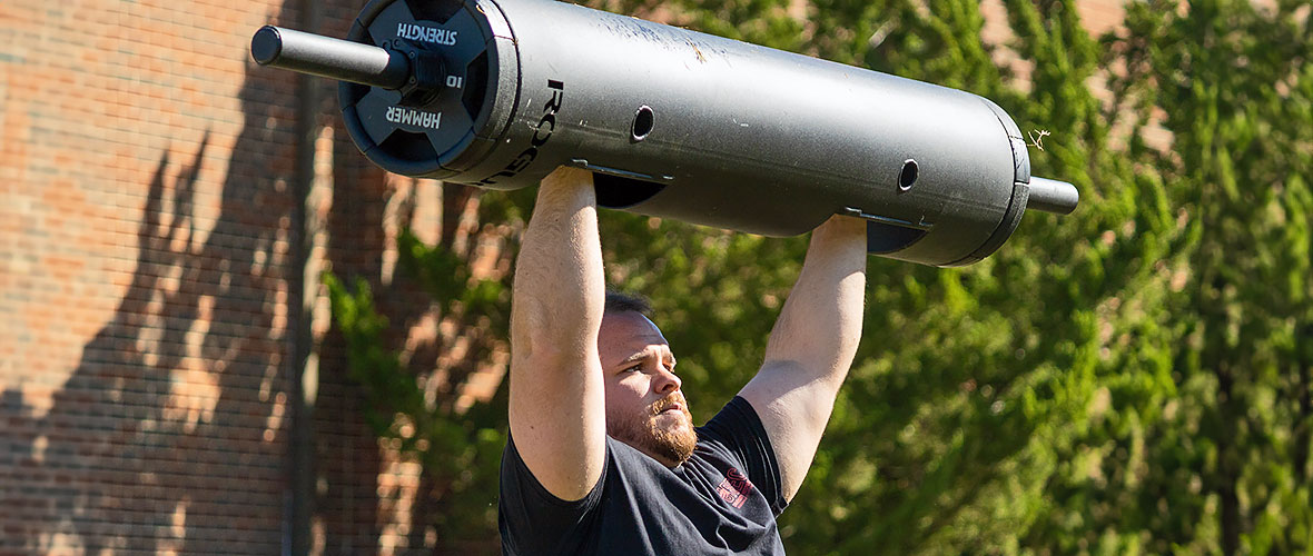 a participant in the Strong Ones competition lifts a heavy metal weight over his head